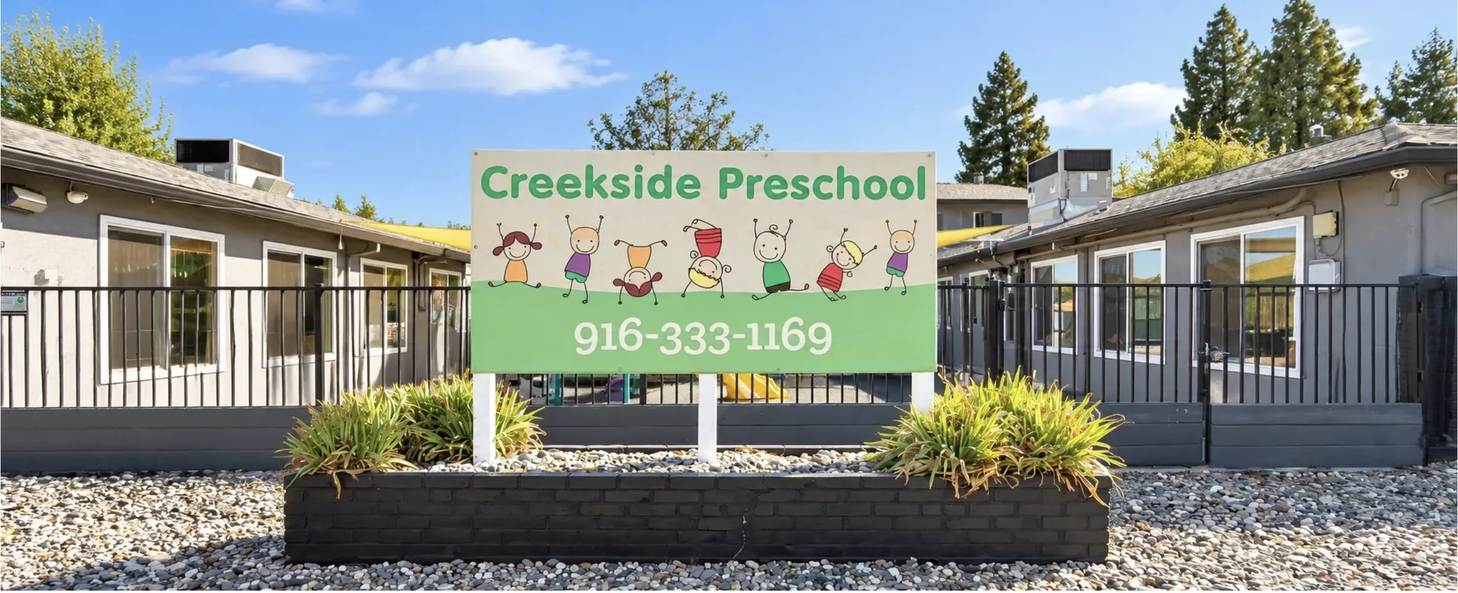 Front of Creekside Preschool: the Creekside Preschool sign with the phone number 916-333-1169 in front of the gray school buildings and fenced playground